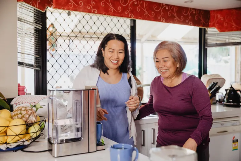 A young woman helps an older woman make a cup of tea with an automatic hot water dispenser