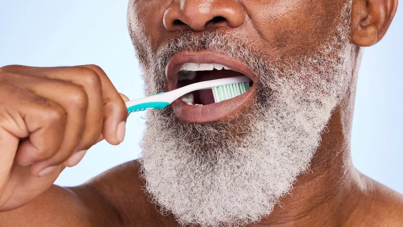 A close up shot of a mature man with a white beard brushing his teeth.