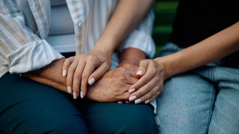 A younger pair of hands clasping an older pair of hands comfortingly.