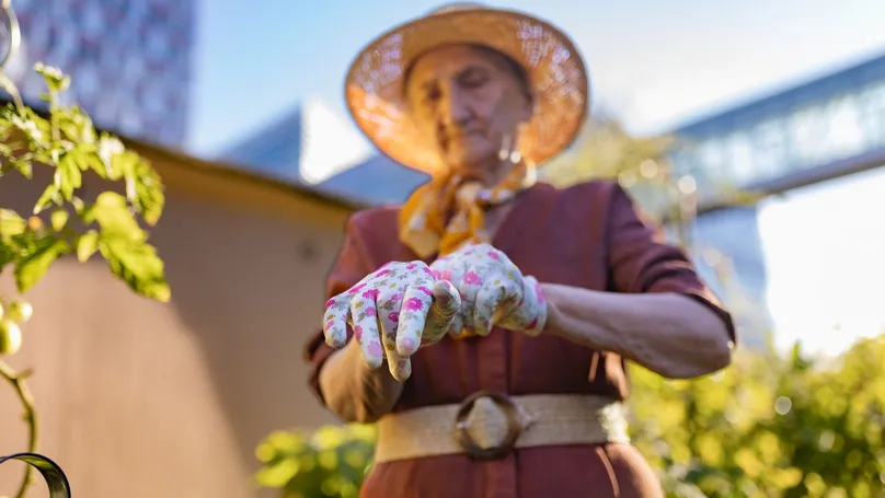A woman in a sunhat puts her gardening gloves on.