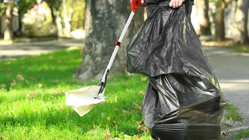 A woman gathers rubbish from her lawn using a long-handled easy reacher tool.