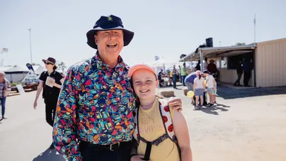 A grandfather and granddaughter standing and smiling together.