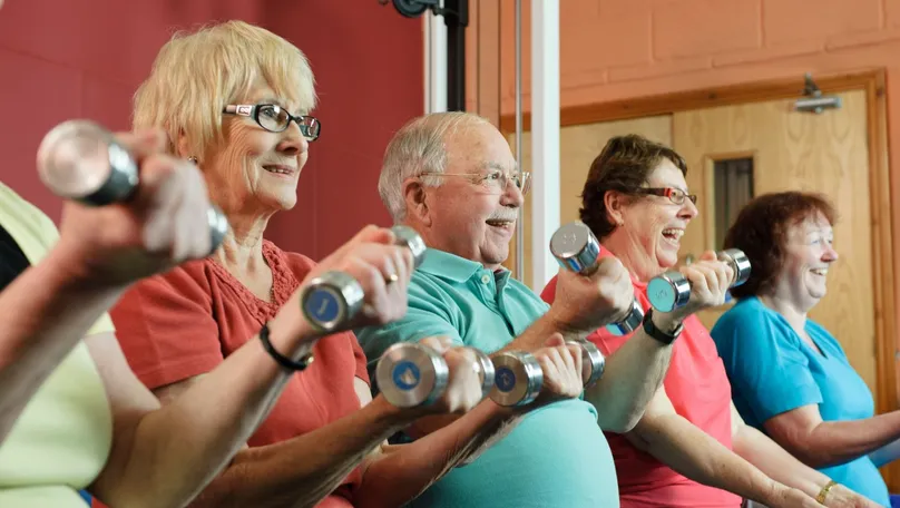 A group of older people lifting dumbbell weights in the gym while laughing.