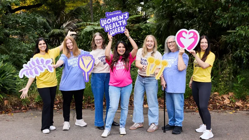 A group of women posing in bright shirts with colourful signs promoting Women's Health Week.