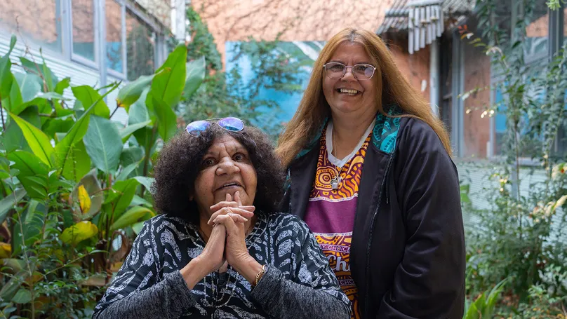 Two First Nations women situated among leafy greenery