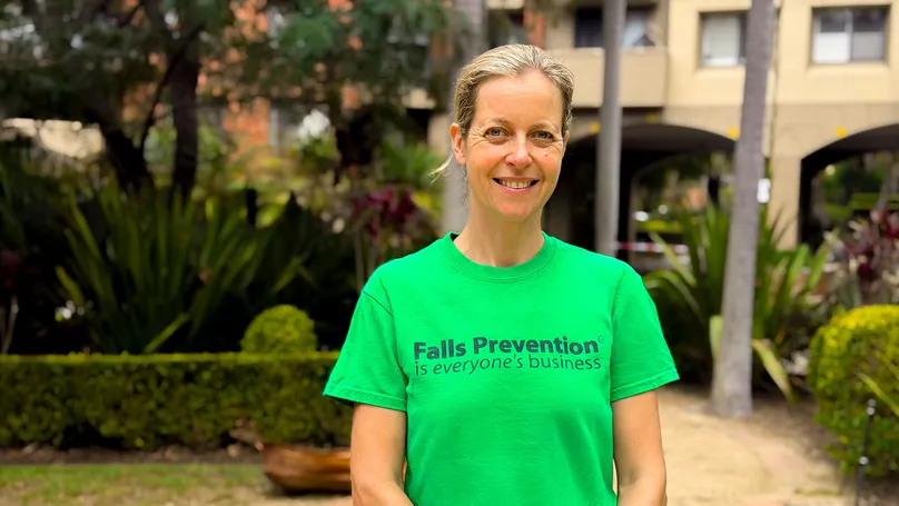 A woman wearing a green T-shirt stands outdoors in a garden courtyard.