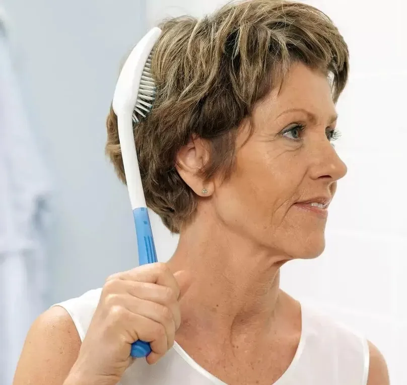 A woman brushing her hair with a long-handled hairbrush.