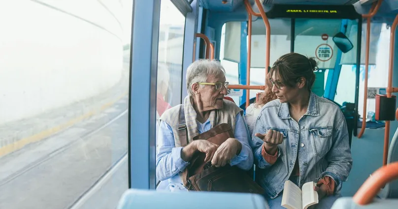 An older man chatting to a woman on the tram.
