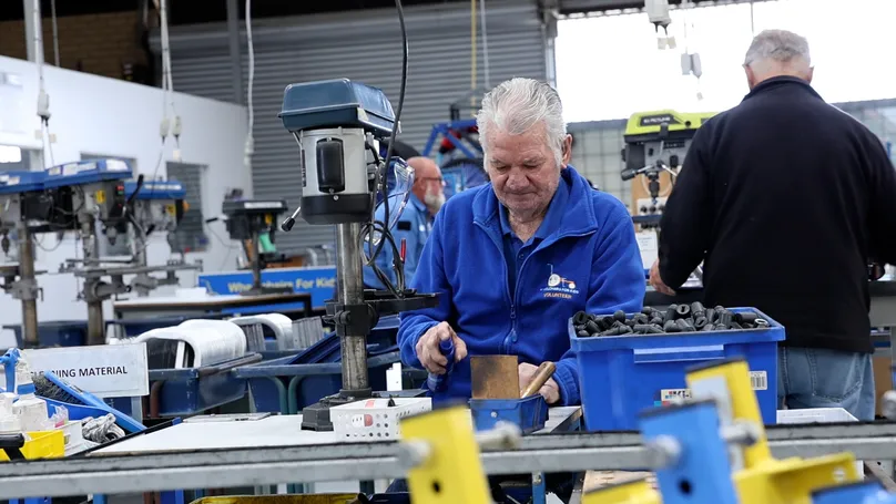 An older man working at a machine in a factory that builds wheelchairs for children.