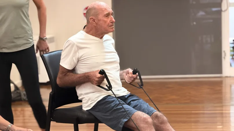 An older man doing the mid row exercise with a resistance band looped under his feet,