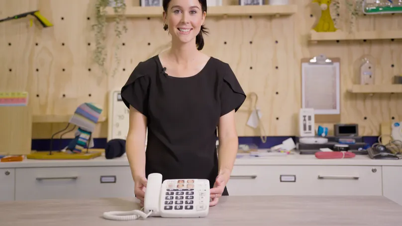 OT Rachel holds an adaptive landline phone with large colourful buttons for demonstrating at Indigo's assistive technology display centre.