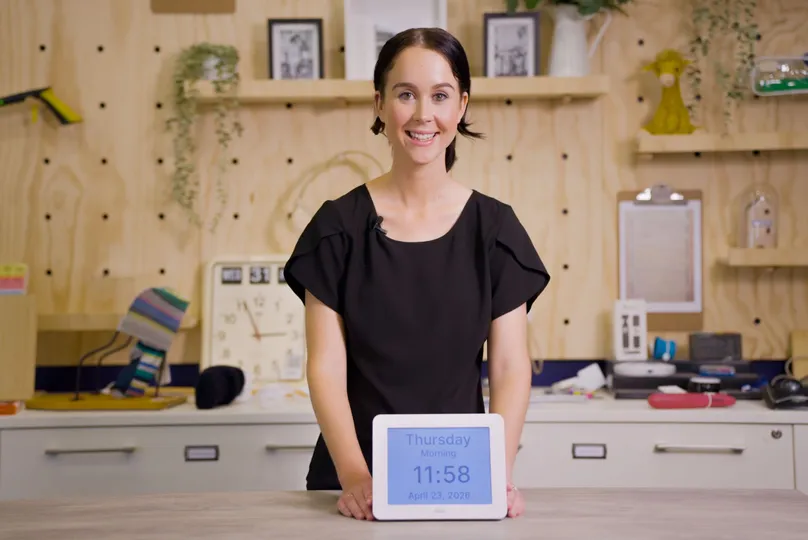 OT Rachel holds a large display digital calendar clock for demonstrating at Indigo's assistive technology display centre.