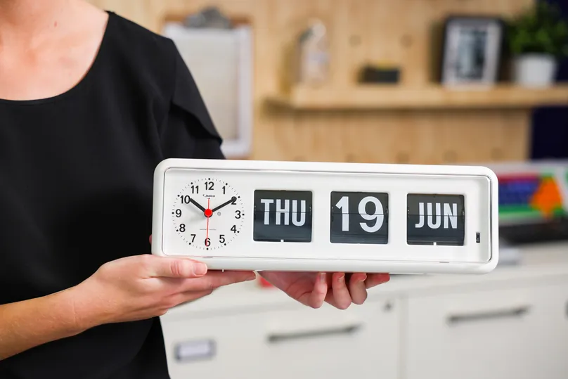 OT Rachel holds a simplified calendar clock with the day, date, and time for demonstrating at Indigo's assistive technology display centre.