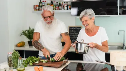 A happy older couple laughing together while chopping fresh vegetables for dinner.