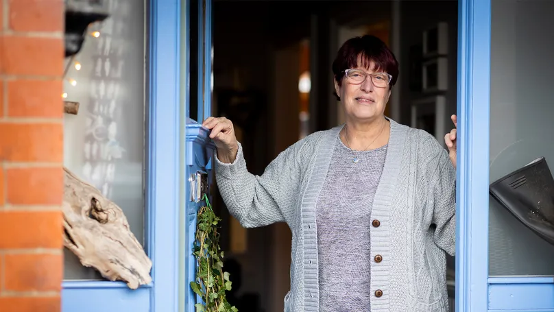 An older woman opening her front door, smiling.