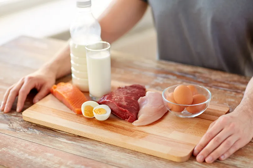 Protein-rich foods including milk, salmon, eggs, and meat on a wooden chopping board.