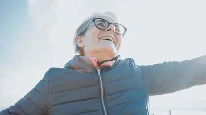 An older woman smiling and embracing the clear sky on her walk outdoors.