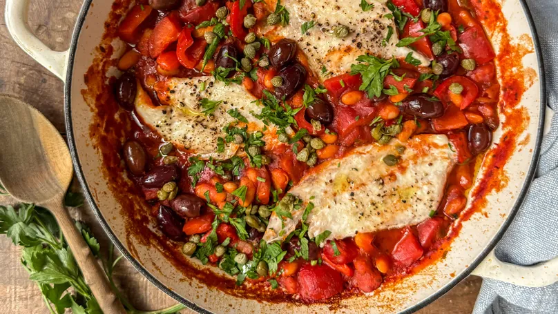 A delicious bowl of snapper and cannellini puttanesca. The sauce is tomato-red, and the garnish is deep green.