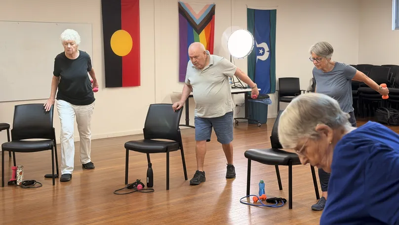 Older people standing with dumbbells, extending their arms back in the second position of the triceps kickback.
