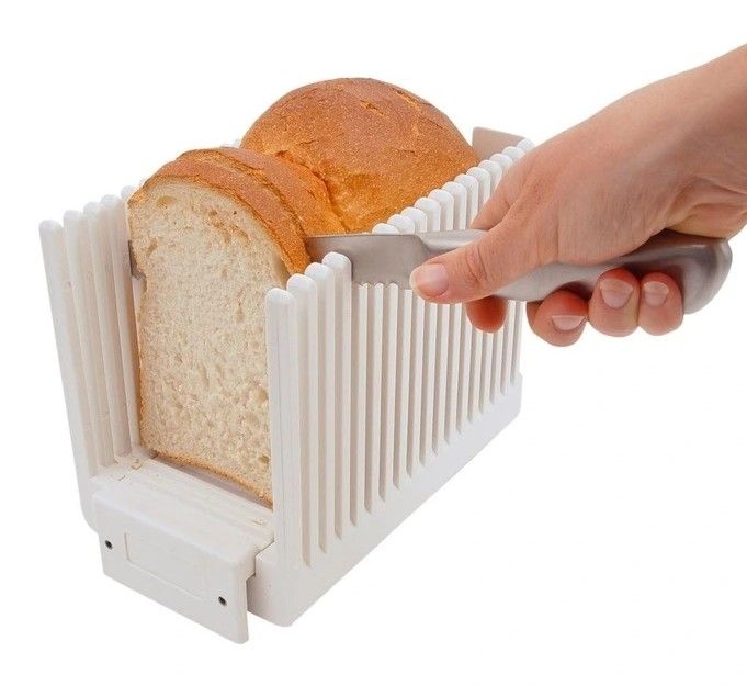 A hand slicing bread with a knife through the slicing guide.