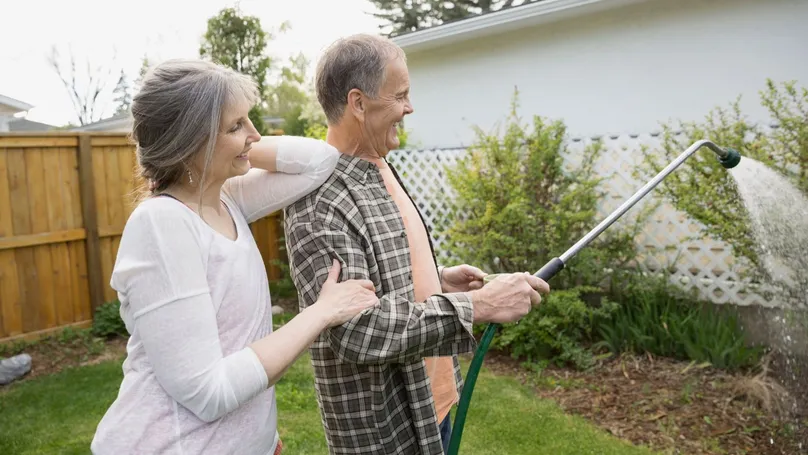 An older couple water the garden with a watering wand.