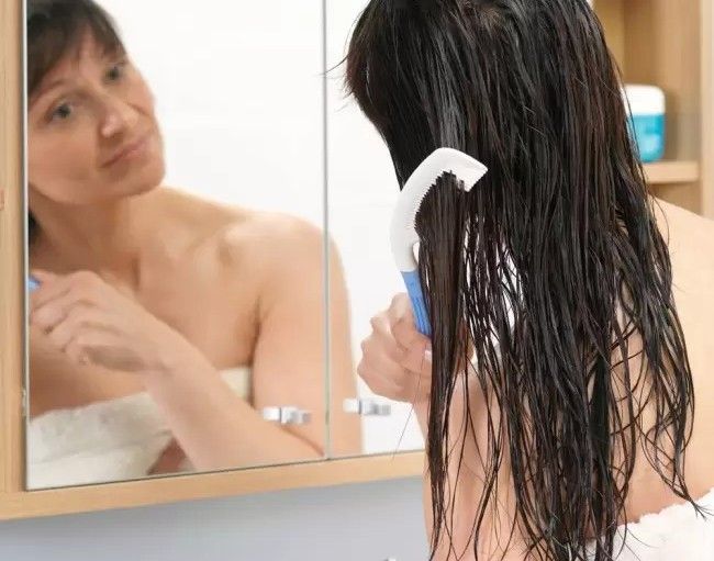 A woman combing her hair with a long-handled comb.