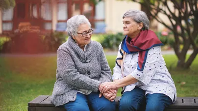 Two older women holding hands while sitting on a park bench.
