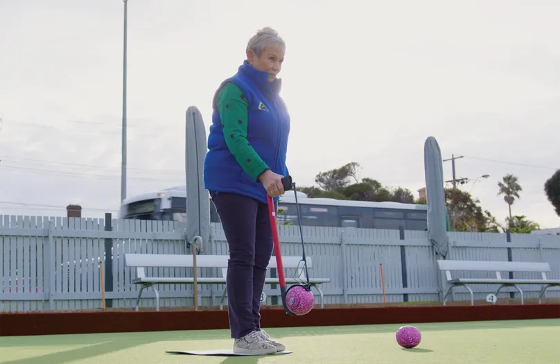 A woman using a bowling arm to play lawn bowls.
