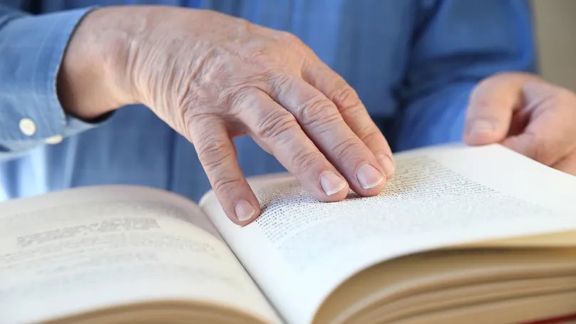 An older man's hands holding open the pages of a large book.