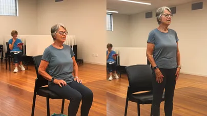 An older woman standing up from a chair.