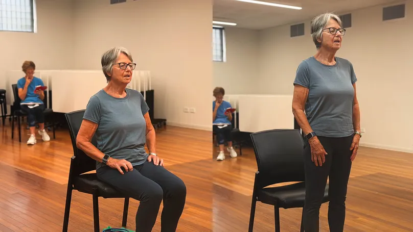 An older woman standing up from a chair.