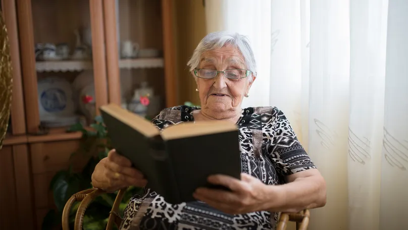 An older woman reading an interesting book at home.